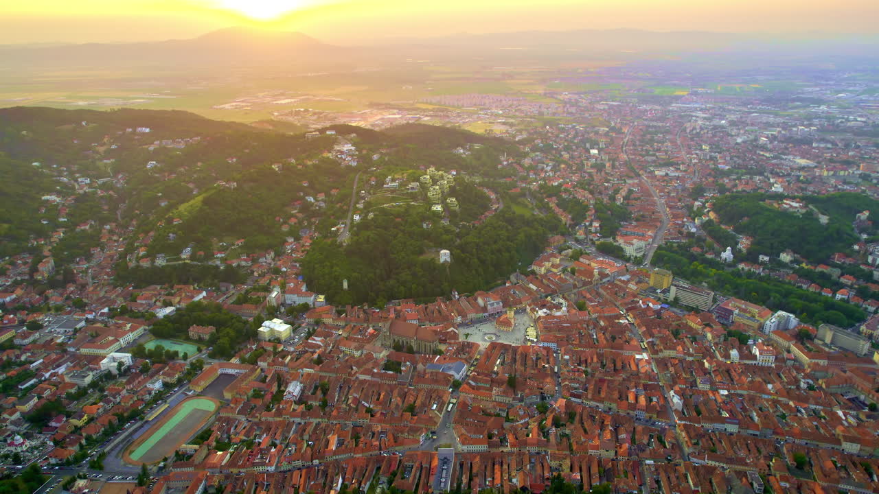 Vista aerea di Brasov al tramonto, Romania, ripresa da un drone. Centro storico con edifici, colline e vegetazione.