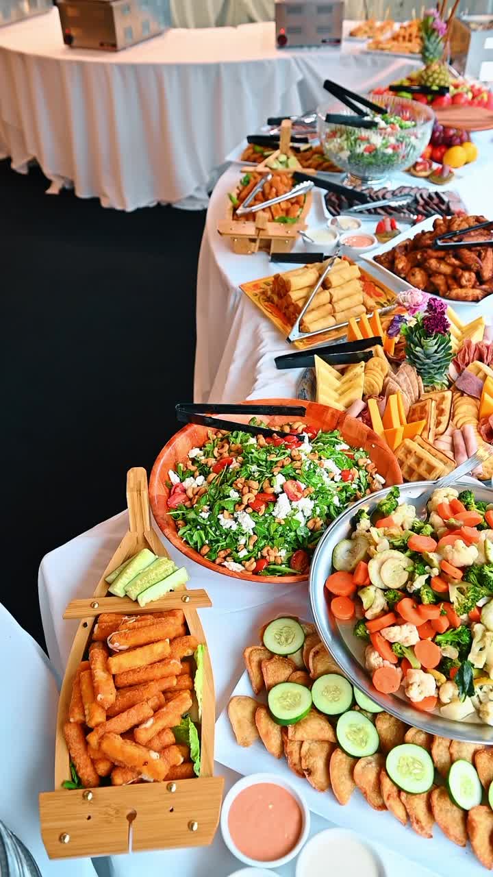 Grande tavolo da buffet per banchetti con una varietà di antipasti e stuzzichini. Un lungo tavolo imbandito con ciotole di insalata, stuzzichini fritti e vassoi di carne.