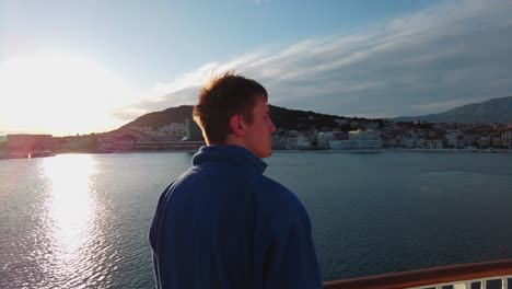 a young, attractive man with dark brown hair and a blue jacket looking at distant objects from the ferry boat which is sailing from split to island vis in croatia, in the adriatic sea 4k uhd