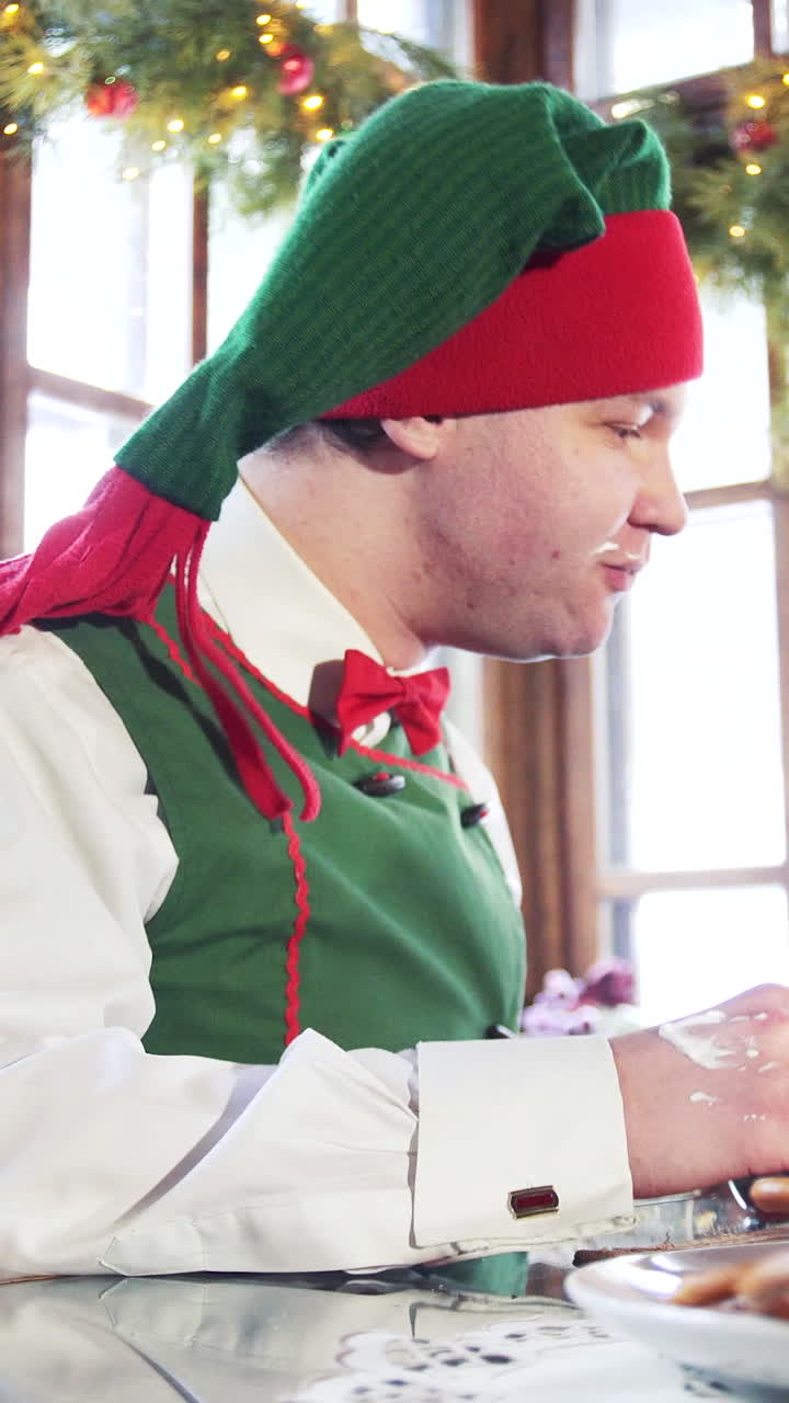 Hungry elf with dirty face and hand eating at the table. Funny man in elf costume quickly eats at Christmas. Vertical video