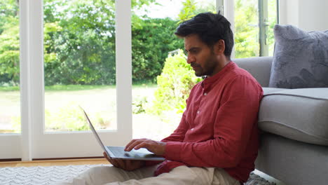 man working from home sitting on floor in lounge using laptop