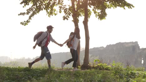 young lovely couple backpackers tourists walking holding hands arrive on hill in front of roman aqueduct arches in parco degli acquedotti park ruins in rome on romantic misty sunrise with guitar and sleeping bag slow motion