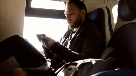 Serious focused European freelance worker typing messages on smartphone messenger app traveling on the train window seat