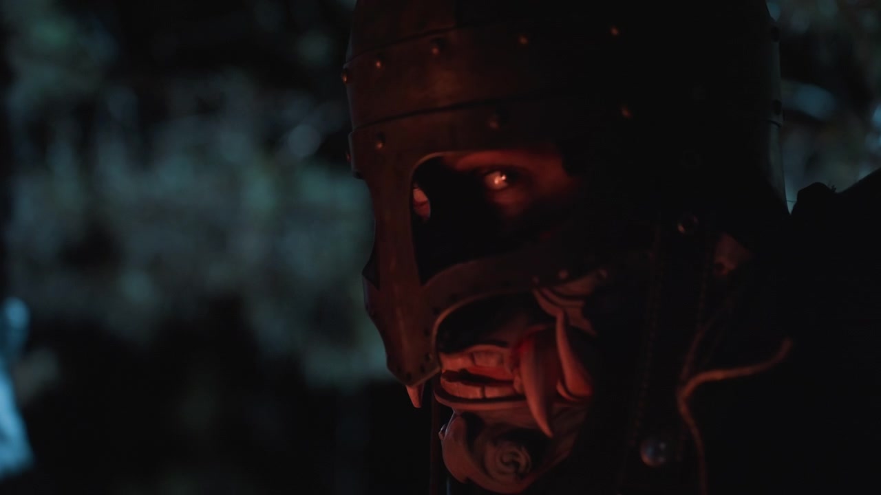 Nighttime off-center close-up shows person in dented medieval-style metal helmet, lower face visible through mouth opening, lips slightly parted, with subtle head turn and tense breathing in dark