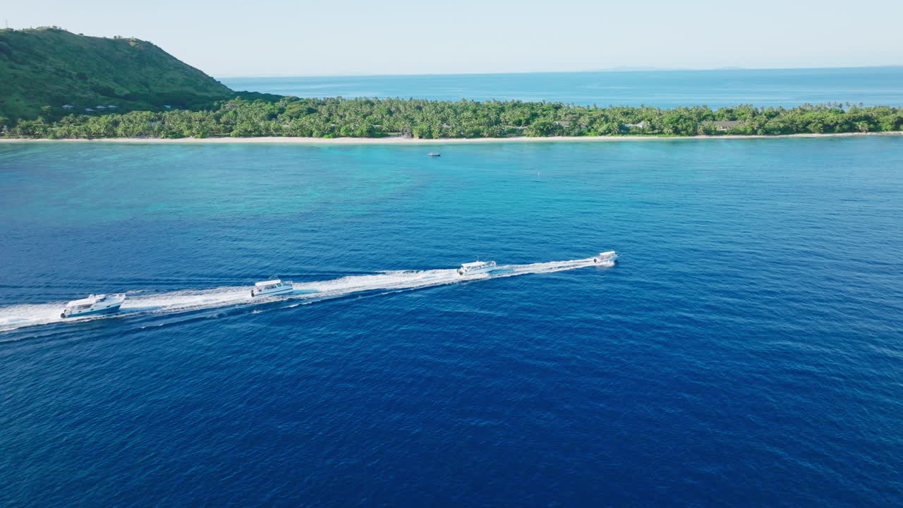 Drone follows tour boat crossing over bright turquoise reef near white sand island