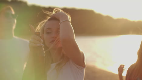 A-young-blonde-girl-is-beautifully-dancing-on-the-beach-party-with-beer-and-friends.-This-is-a-carefree-summertime-on-the-open-air-party.