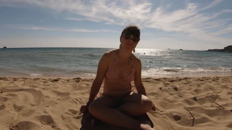 A-girl-sitting-on-sand-on-a-sunny-sandy-beach-in-Greece