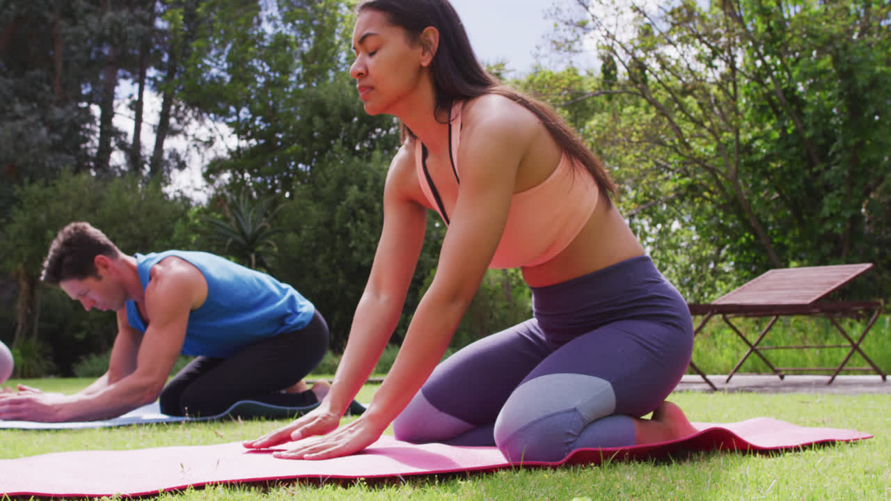 un grupo diverso de hombres y mujeres practicando yoga se arrodillan en esteras en el parque