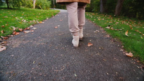 a woman walks along a path in an autumn park, only her legs are visible in the frame.