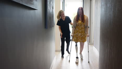 woman with prosthetic leg walking using crutches with therapist in hallway, copy space
