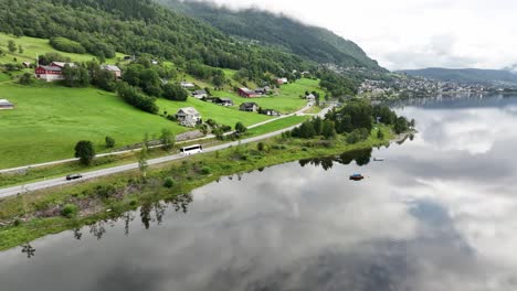 Aerial-following-white-bus-driving-road-E16-towards-city-of-Voss-with-Vangsvatnet-lake-on-the-side---Voss-Norway-in-background---Aerial