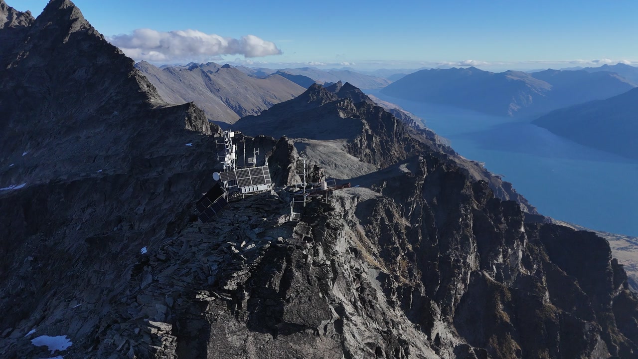 Aerial orbits communication tower on mtn peak above Lake Wakatipu, NZ