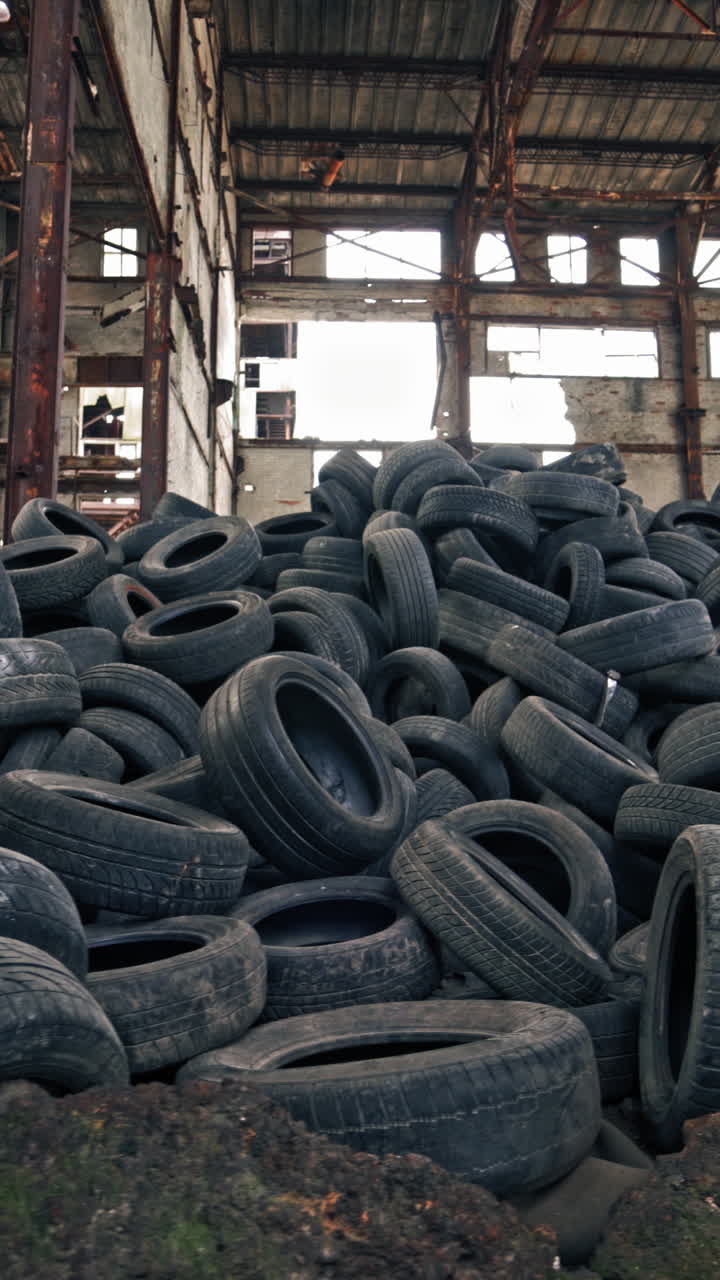 Black junk tires lying on the floor in the old abandoned building. Many used rubber tires from different vehicles are on a desolate plant inside. Vertical video