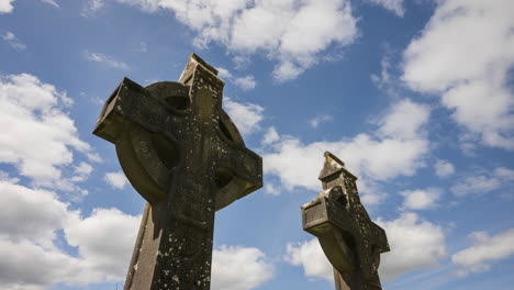 lapso de tiempo de la cruz de piedra medieval tradicional del cementerio histórico en las zonas rurales de irlanda con nubes pasajeras y sol