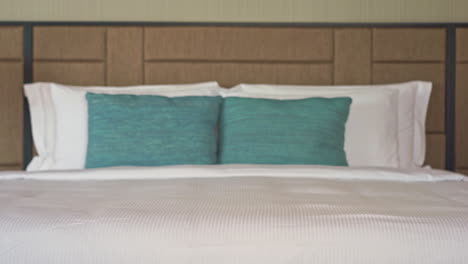 tilt up of a luxurious bed in the room of a resort with white duvet and aqua pillows