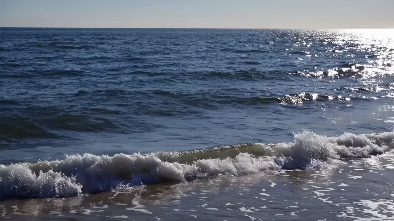 Video rilassante di una spiaggia con inquadratura dal basso che cattura onde dolci e la luce solare scintillante.