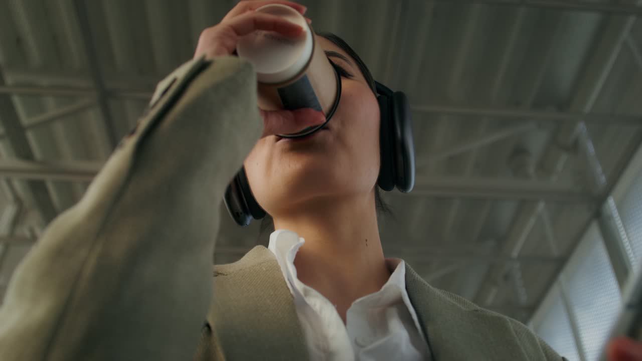 여자가 기차역에서 커피를 마시고 음악을 듣고 있다