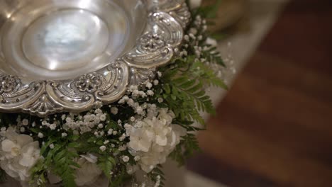 Ornate-silver-baptismal-font-adorned-with-white-flowers-and-greenery,-symbolizing-purity-and-faith