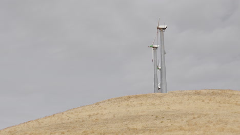 Kleine-Gruppe-Von-Windmühlen-Dreht-Sich-Nicht-Auf-Einem-Trockenen-Hügel,-Während-Die-Wolken-Langsam-Vorbeiziehen