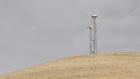 un pequeño grupo de molinos de viento que no giran en la colina seca a medida que la nube pasa lentamente