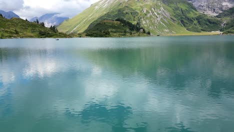 calm water of an alpine lake with reflection of sky clouds and swiss mountains behind, aerial drone view, obwalden, engelberg