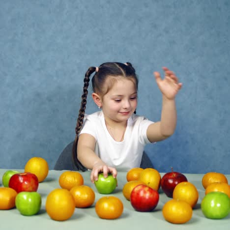 cheerful kid with fresh fruits. little girl sitting at the table full of ripe organic fruits. healthy food concept.
