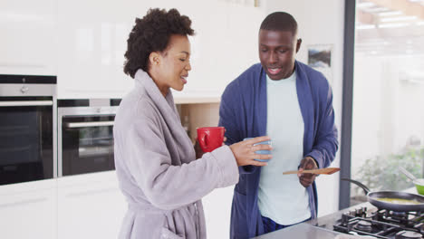 Video-of-happy-african-american-couple-preparing-breakfast-and-coffee-together-in-kitchen