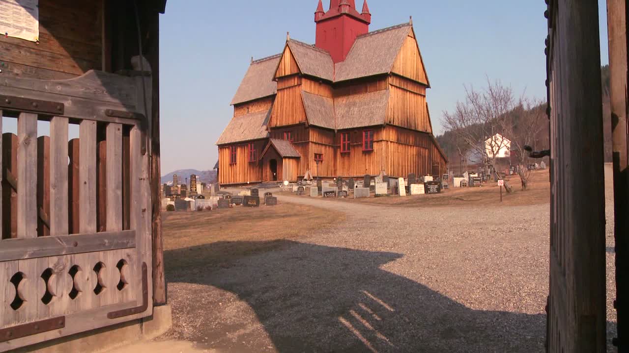 incline hacia arriba a través de una puerta frente a una antigua iglesia de madera en noruega