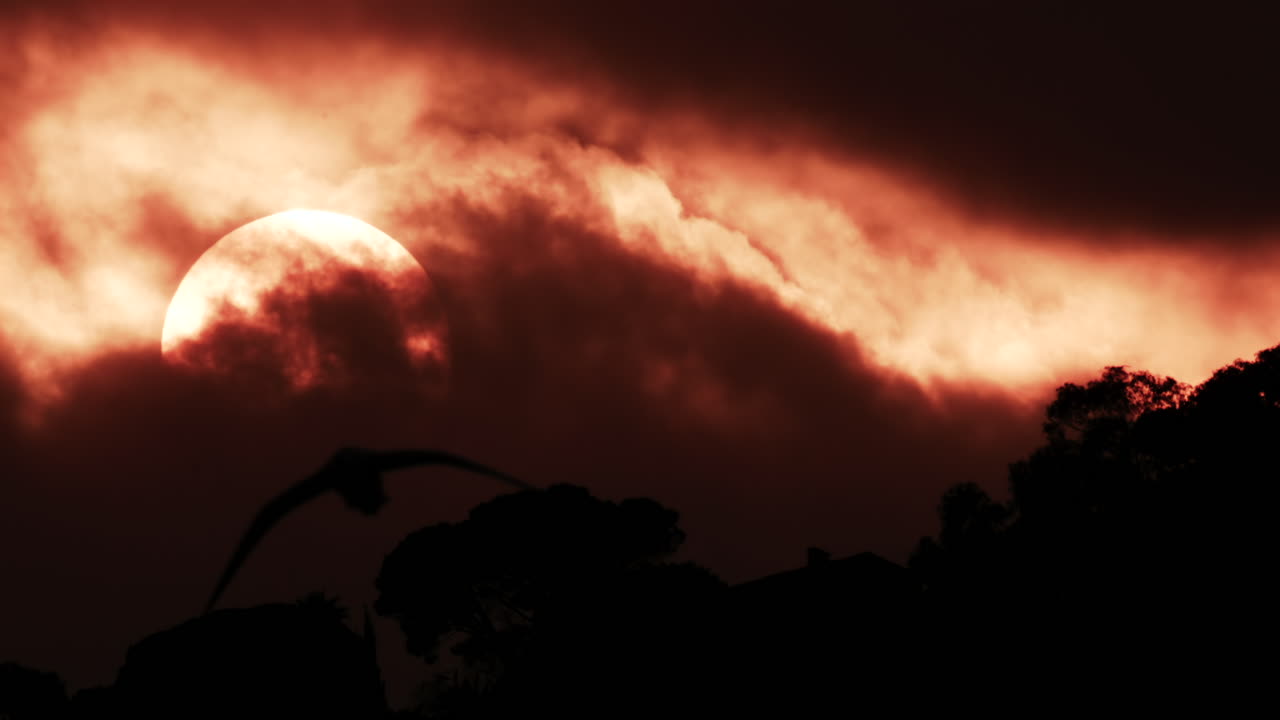 A glowing red sun partially covered by dark clouds at dusk