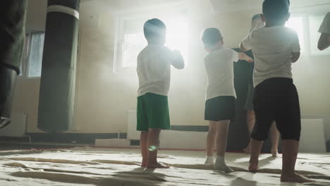 children do hits with instructor at boxing school. little fighters exercise strong punches with professional trainer in gym slow motion. self-defence lesson