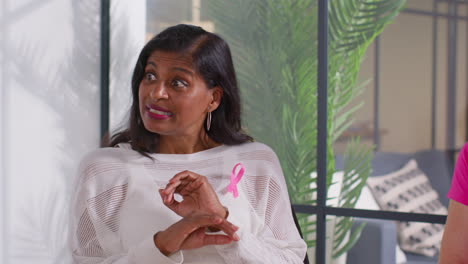 mature woman wearing pink breast cancer awareness ribbon talking at meeting of therapy support group for cancer treatment patients 2