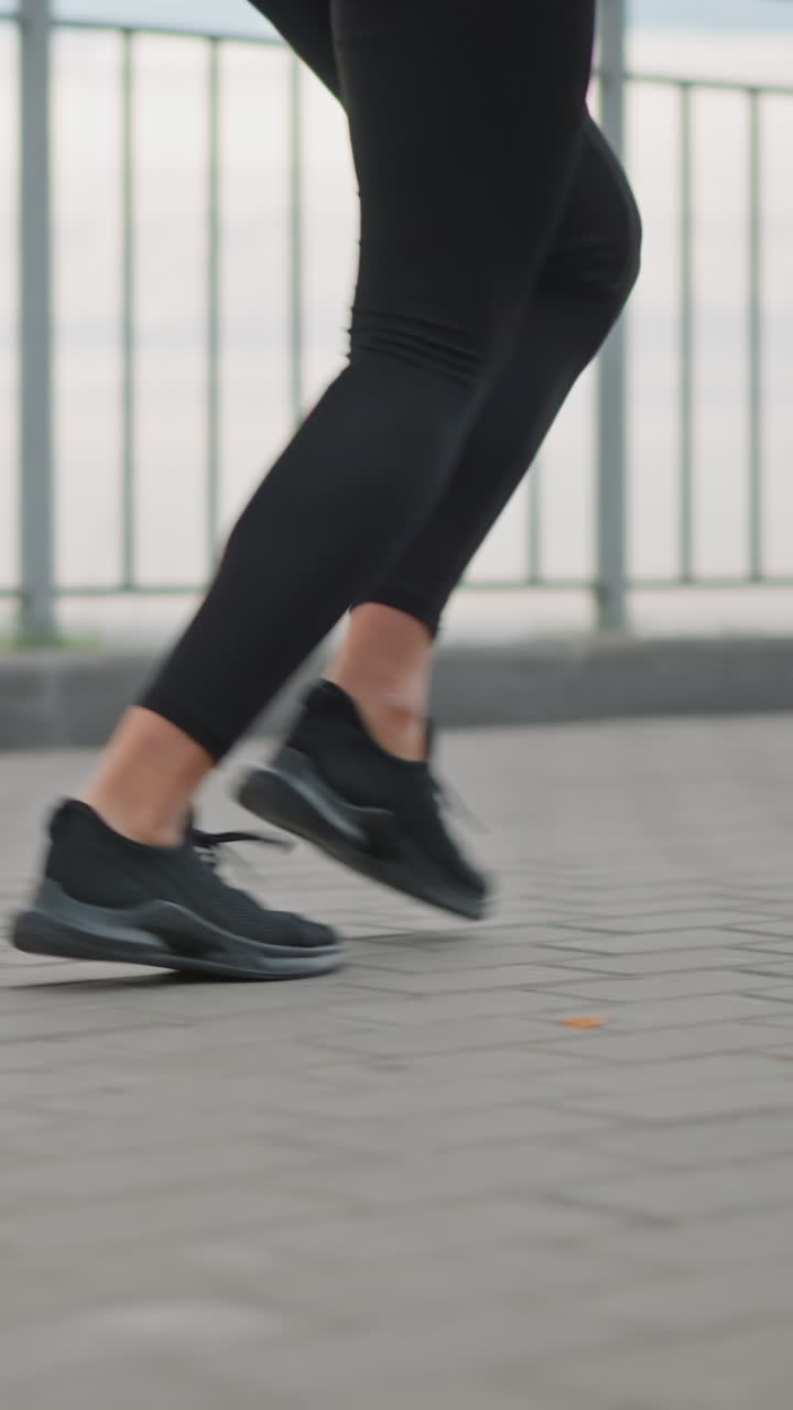 Close-up view of woman's legs in black leggings and black sneakers jogging on paved pathway next to iron fence, showcasing athletic movement outdoors fitness