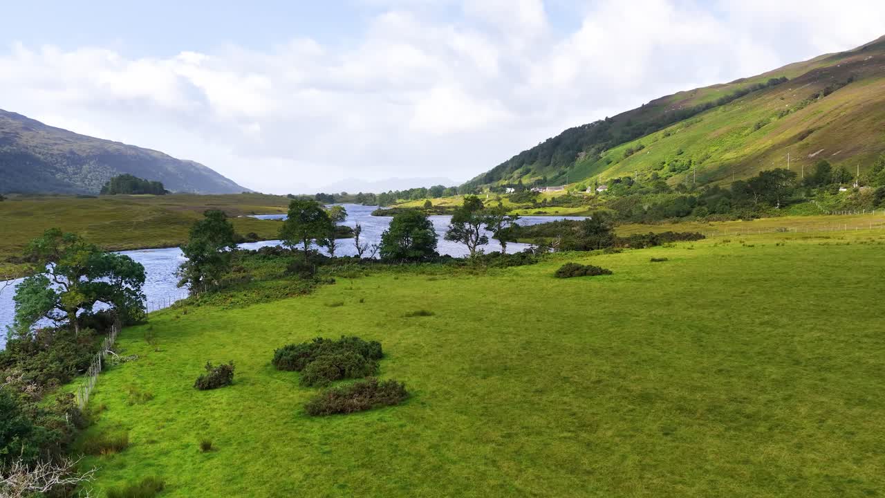 Drone glides above green river valley, meadows, and hills under soft daylight, tranquil countryside scene