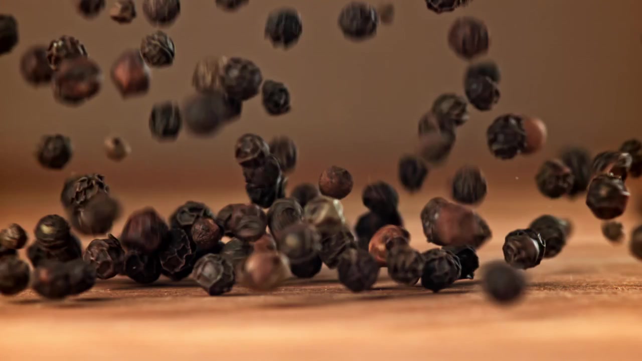 Svarte pepperkorn som faller og spretter på en treoverflate i sakte film