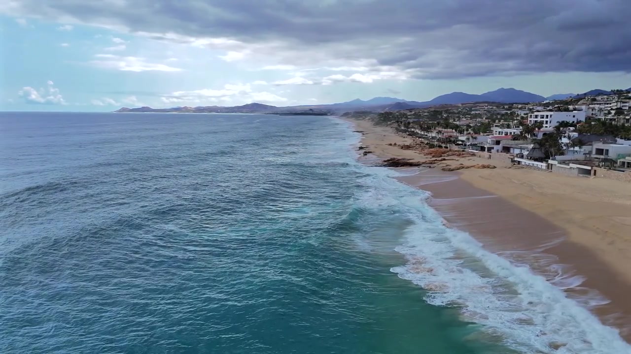 Drone voa sobre o oceano em La Laguna, seguindo as ondas enquanto elas chegam e quebram abaixo, girando para manter Palmilla Point no enquadramento ao longo da costa.