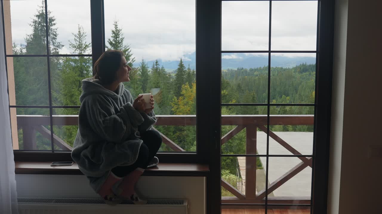 산을 볼 수 있는 창문 에서 커피를 마시고 있는 여자