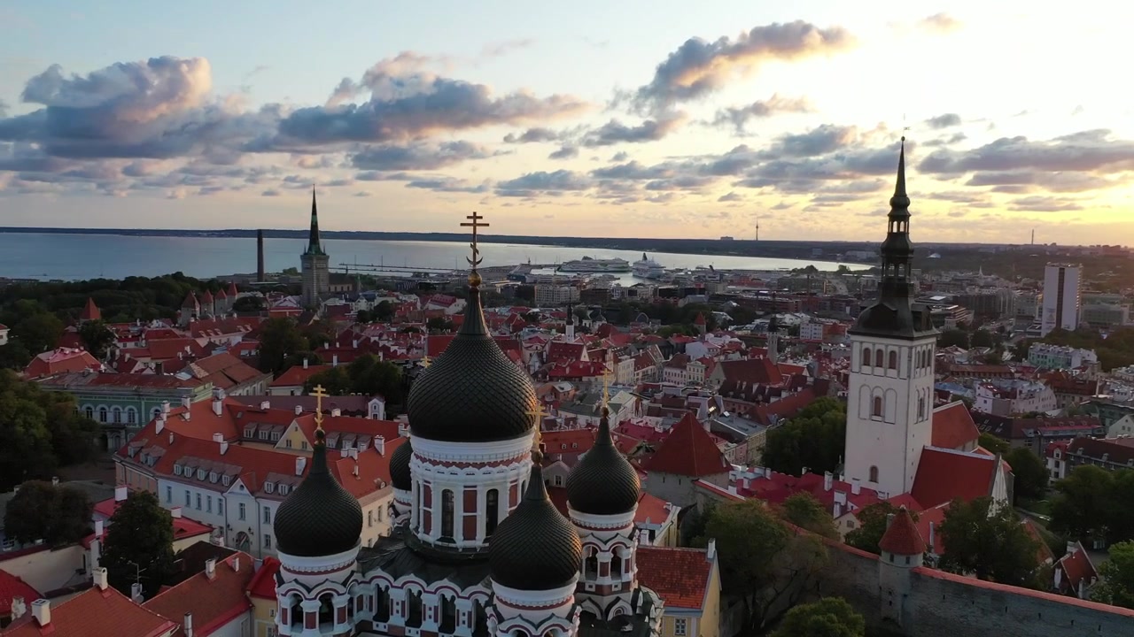 Impresionantes imágenes de dron del casco antiguo medieval de Tallin al atardecer. La toma muestra la colina de Toompea, la Catedral de Santa María y edificios con tejados rojos bajo un cielo dramático de nubes rosas y naranjas.