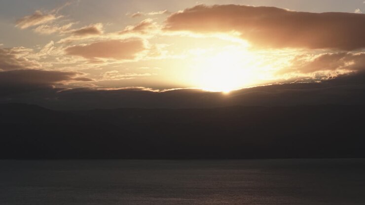 Vista cinematografica dei raggi dorati del sole che penetrano tra le nuvole di una forte tempesta sul Mar Morto e sui monti della Giordania durante un cupo tramonto invernale