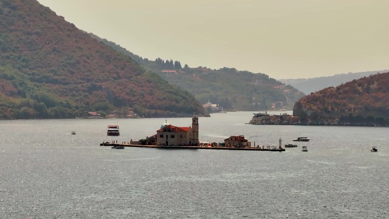 Il monastero di Otocic Sveti Dorde si trova su una piccola isola mentre barche turistiche e piccole imbarcazioni si muovono attraverso il tranquillo canale della baia