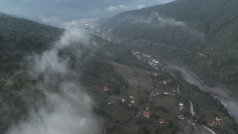 fly over clouds river stream houses and lush dark forest tree in the balkans