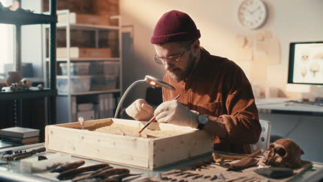 archaeologist uncovering artifact in sand box during lab research