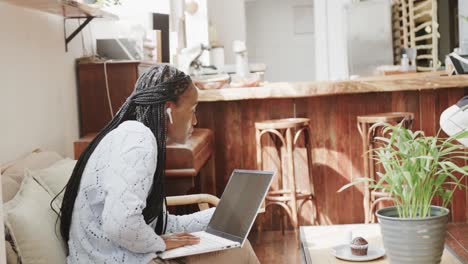 African-american-woman-using-laptop-and-drinking-coffee-sitting-in-coffee-shop,-slow-motion