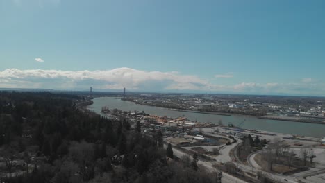 scenic view of delta bc on the edge of the fraser river with the alex fraser bridge in the background bright day blue sky clouds aerial wide reversing revealing neighbourhood next highway