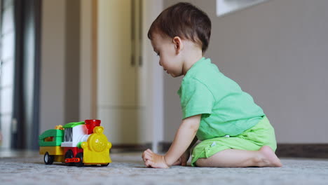 cute baby boy presses button persistently on his toy. adorable kid watches the toy train moves away and smiles. low angle view.
