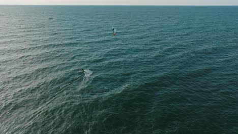 Establishing-aerial-view-of-a-group-of-people-engaged-in-kitesurfing,-sunny-summer-day,-high-waves,-extreme-sport,-Baltic-Sea-Karosta-beach-,-wide-birdseye-drone-shot-moving-forward