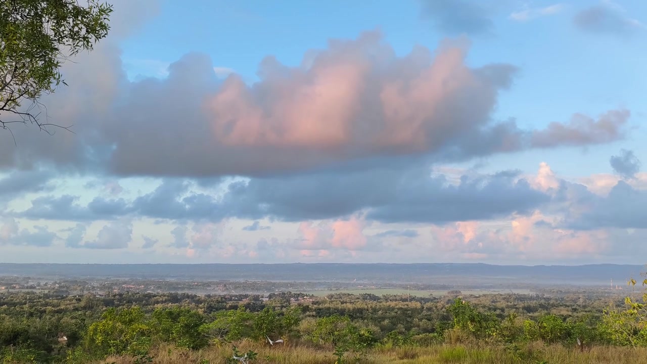 Panoramaudsigt over frodig dal under pastelfarvede solnedgangsskyer