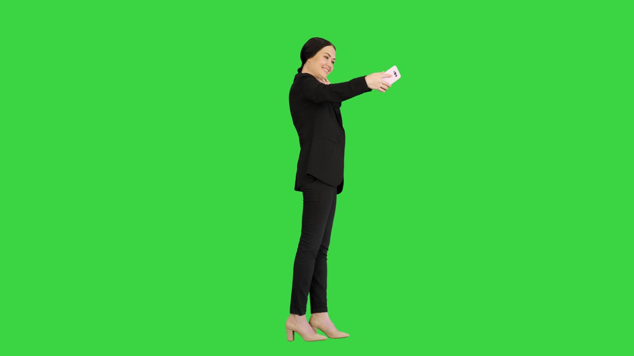 미소 짓는 사업가 여성이 초록색 화면, 크로마 키에서 셀피를 찍고 있습니다.