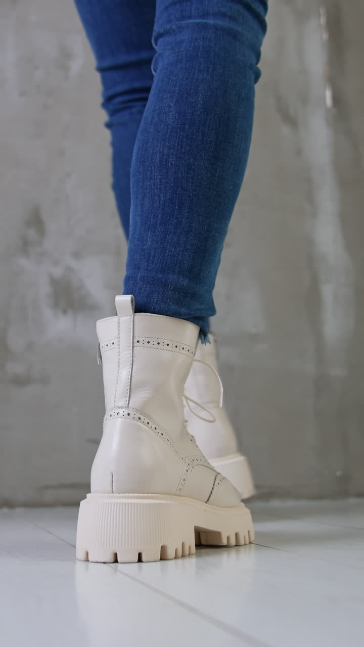 Model in blue jeans shows white boots on tractor soles. Close up. Studio footwear presentation. Low angle view. Vertical video