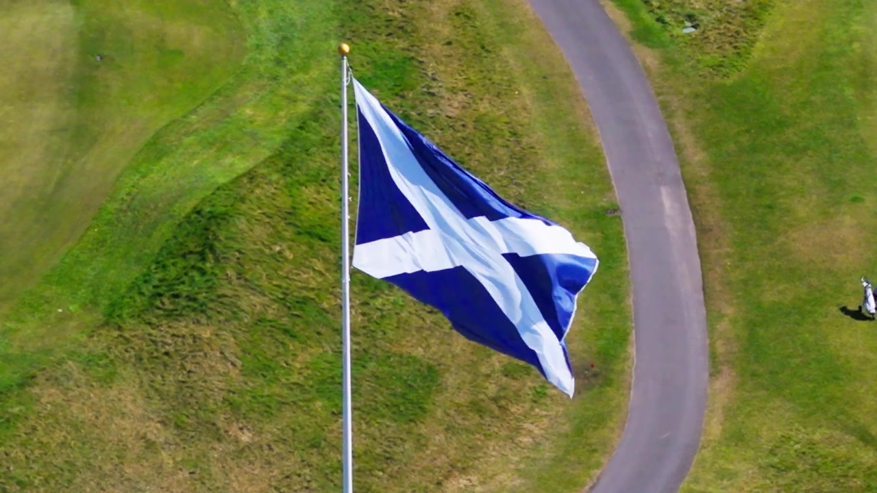 Filmisk luftfoto af det skotske Saltire-flag, der vajer i vinden på Skotlands vestkyst, og viser national stolthed, kulturarv og naturskønne rejser