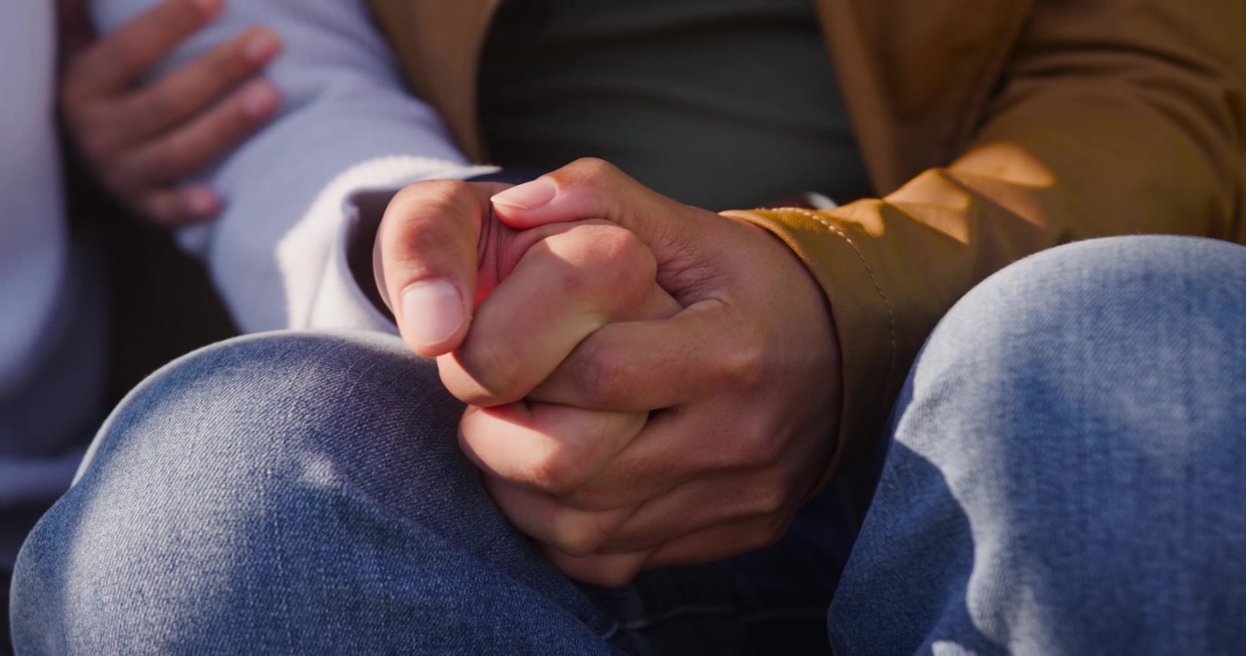 Pareja afroamericana con las manos entrelazadas sobre rodillas de mezclilla, los dedos relajándose para mayor comodidad
